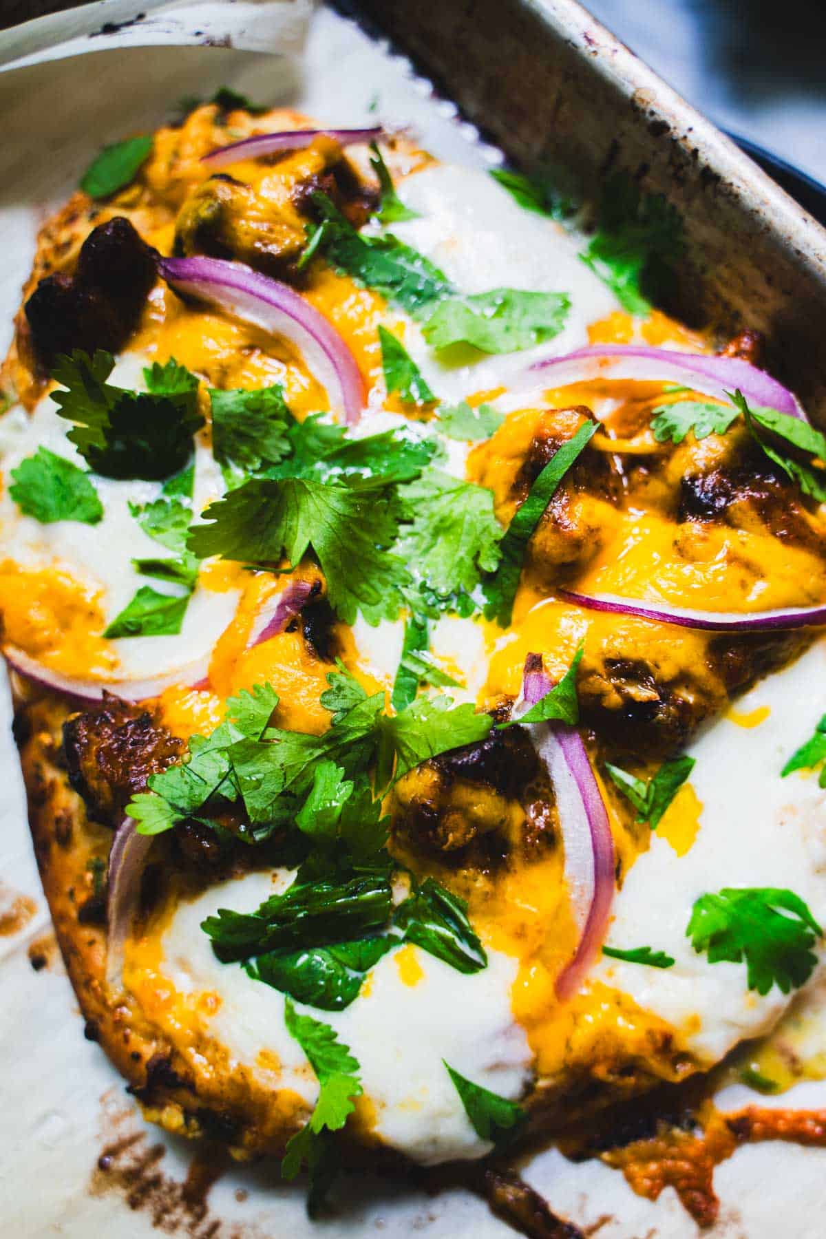 Baked butter chicken on garlic naan pizza garnished with cilantro on a baking sheet.