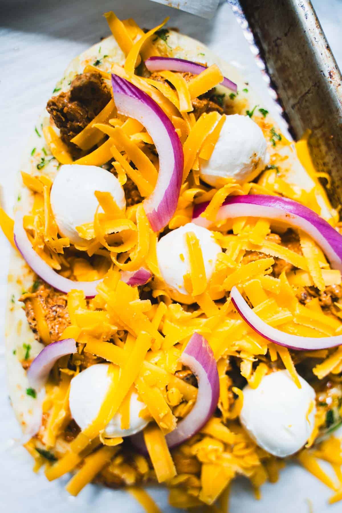 Shredded cheddar cheese, small mozzarella balls and thin slices of red onion on top of naan.