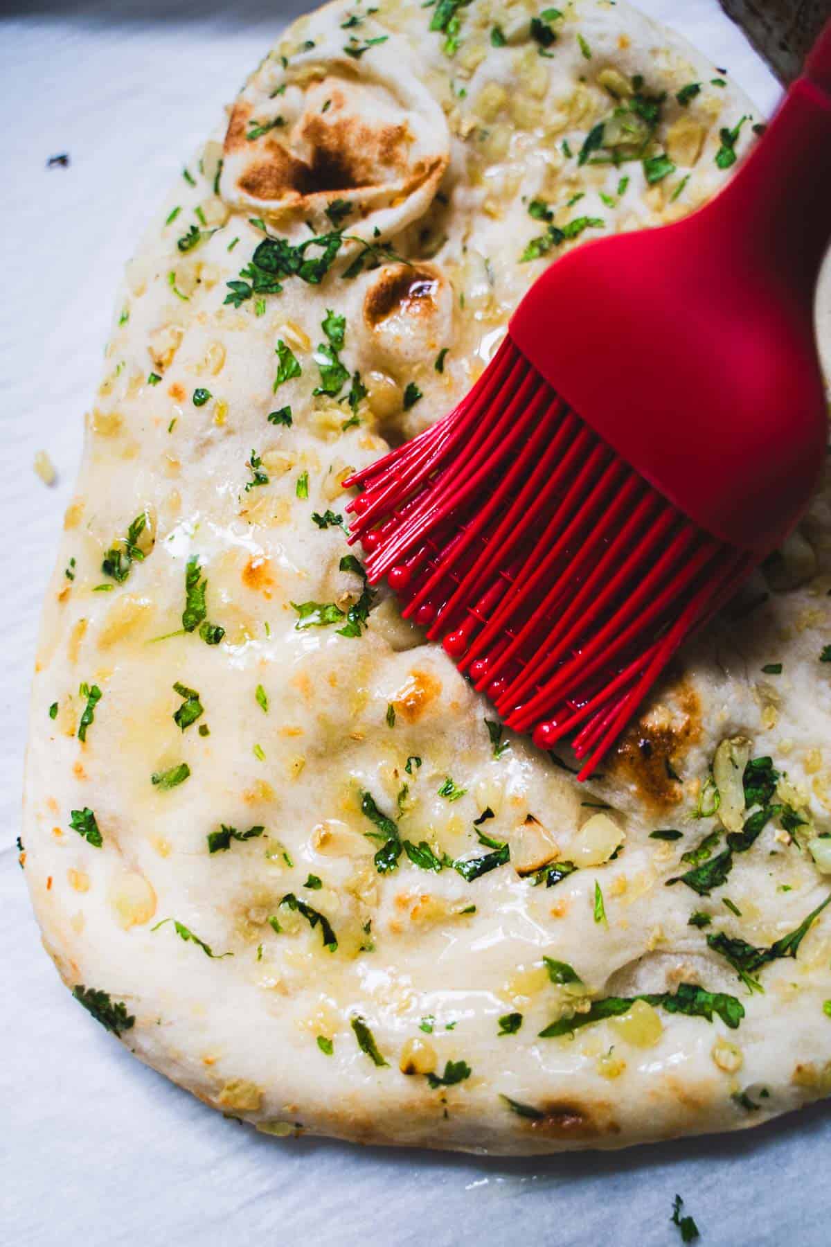 Red pastry brush, brushing on garlic butter over top of naan on a baking sheet.