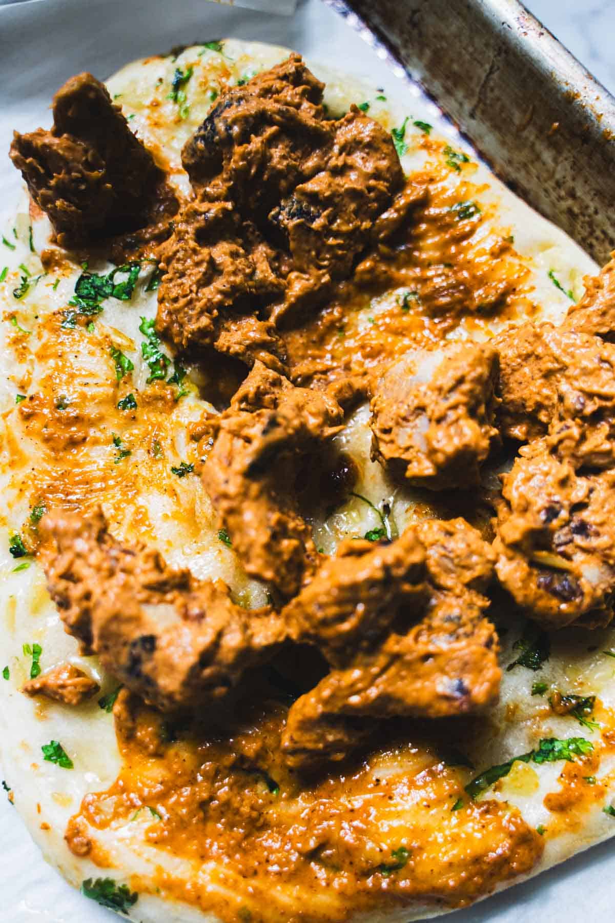 Butter chicken spread over warmed garlic naan on a baking sheet to make Naan pizza.