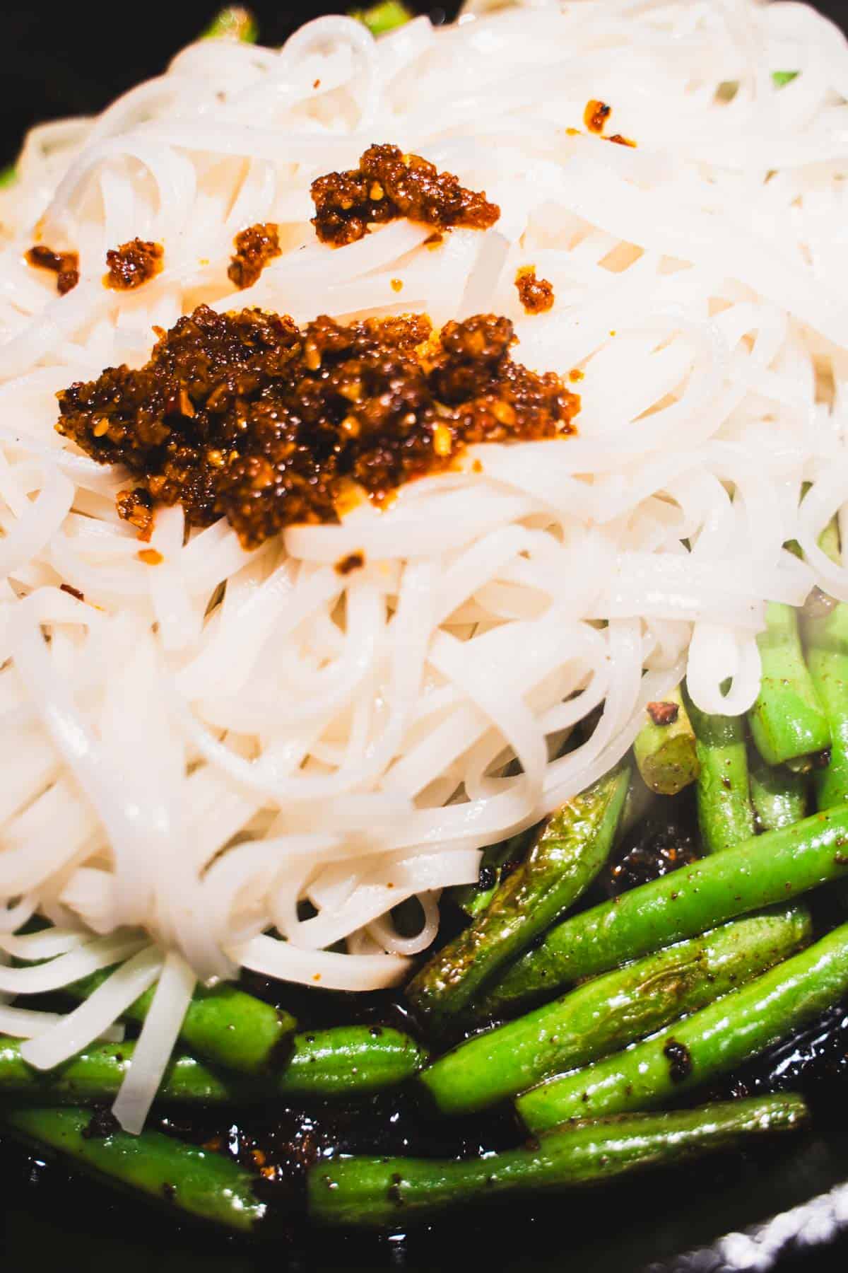 Rice noodles tossed into cast iron skillet with green beans, garnished with chili crisp.