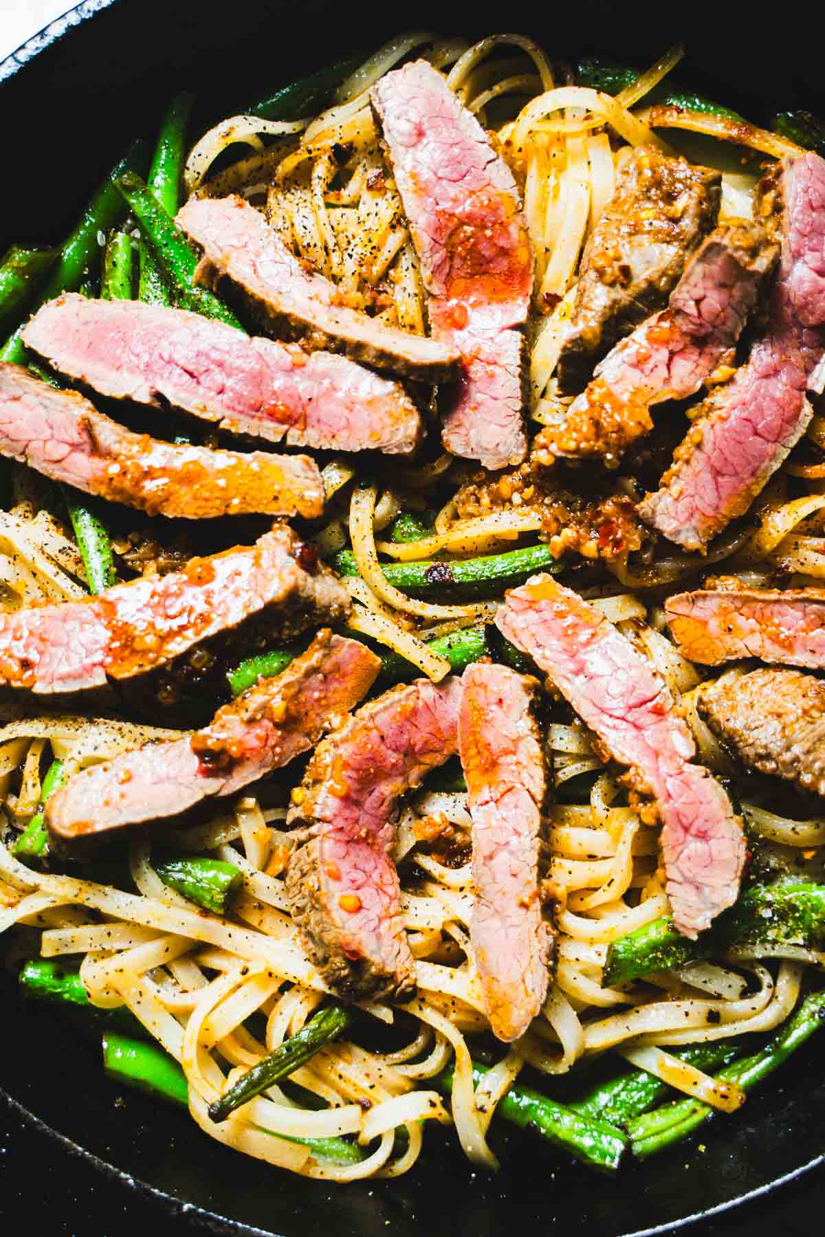 Flank steak added to noodles and green beans in a cast iron black skillet.