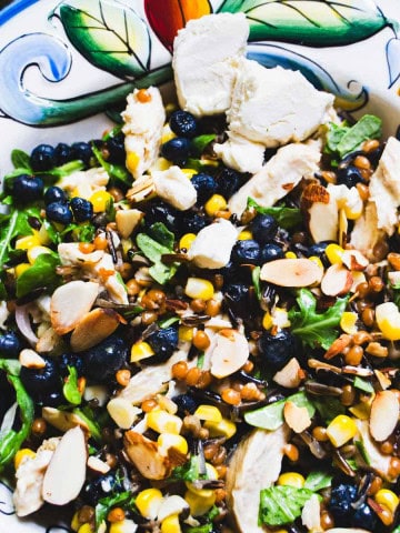 Wheat berry and wild rice grain bowl with pickled corn and blueberries in a decorated bowl and a salad bowl with wheat berries and wild rice in glass jars.