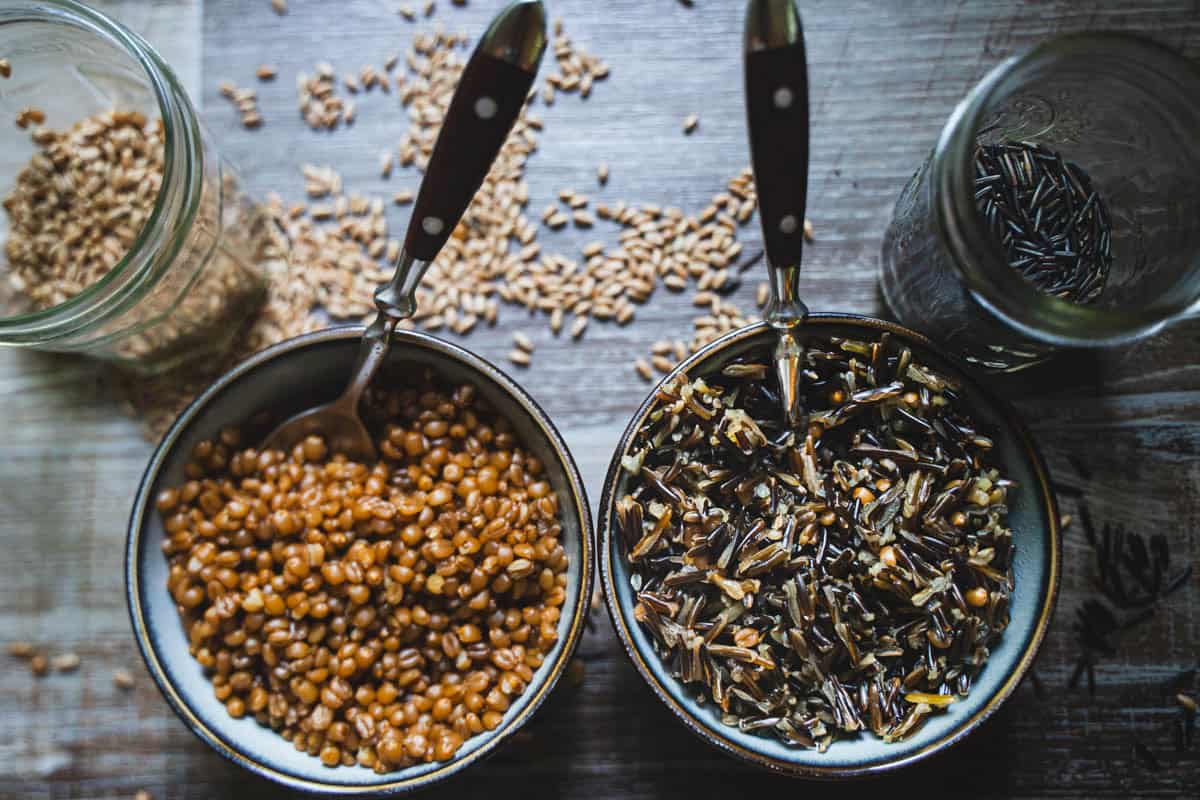 uncooked and cooked wheat berry and wild rice in glass jars and bowls.
