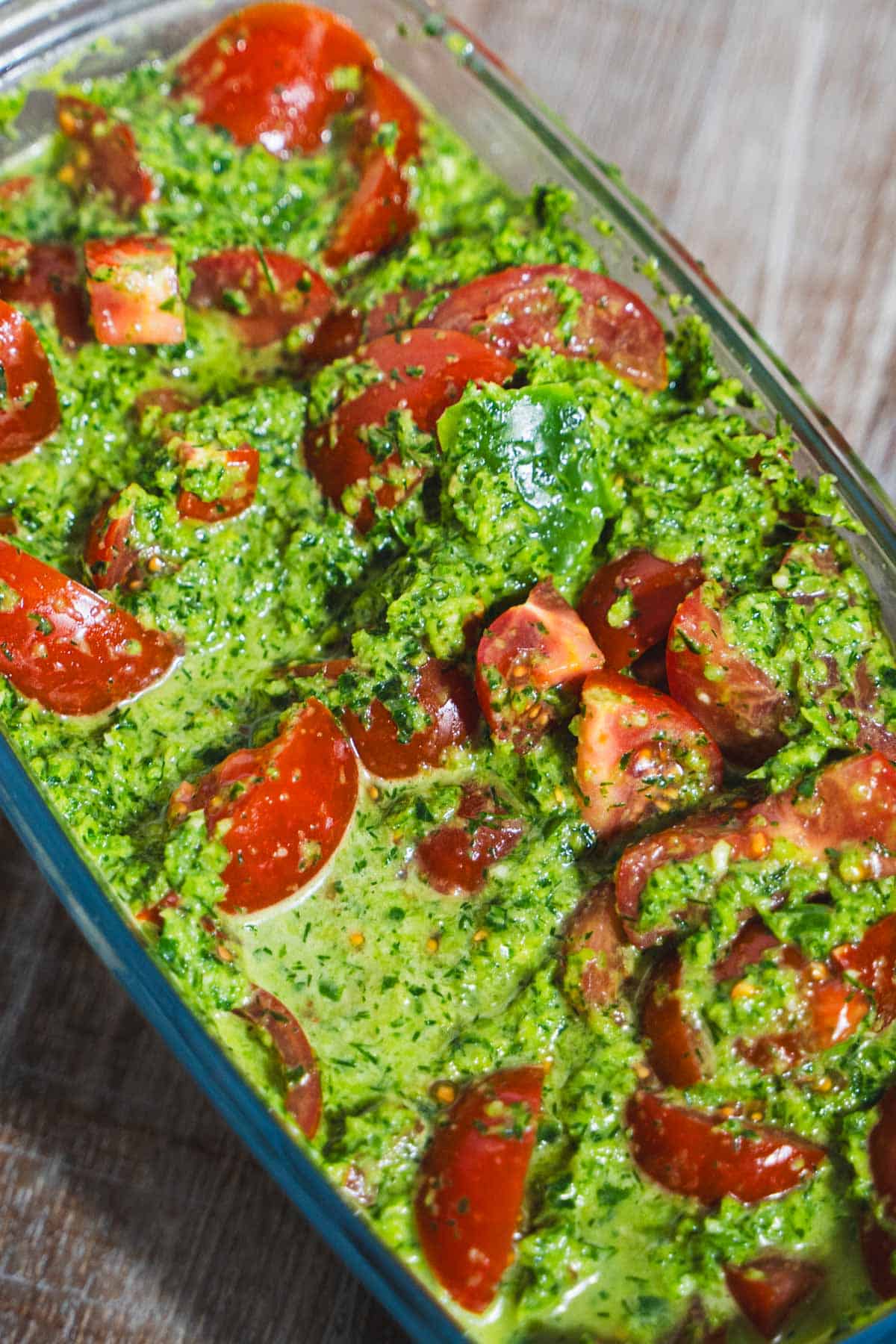 Marinated tomatoes in a glass rectangle loaf pan on wooden table.