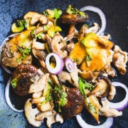 Mushroom salad tossed with pickled mushrooms, roasted mushrooms, celery, cilantro, red onions and a vinaigrette on a black plate next to cherry tomato bruschetta and sprigs of basil.