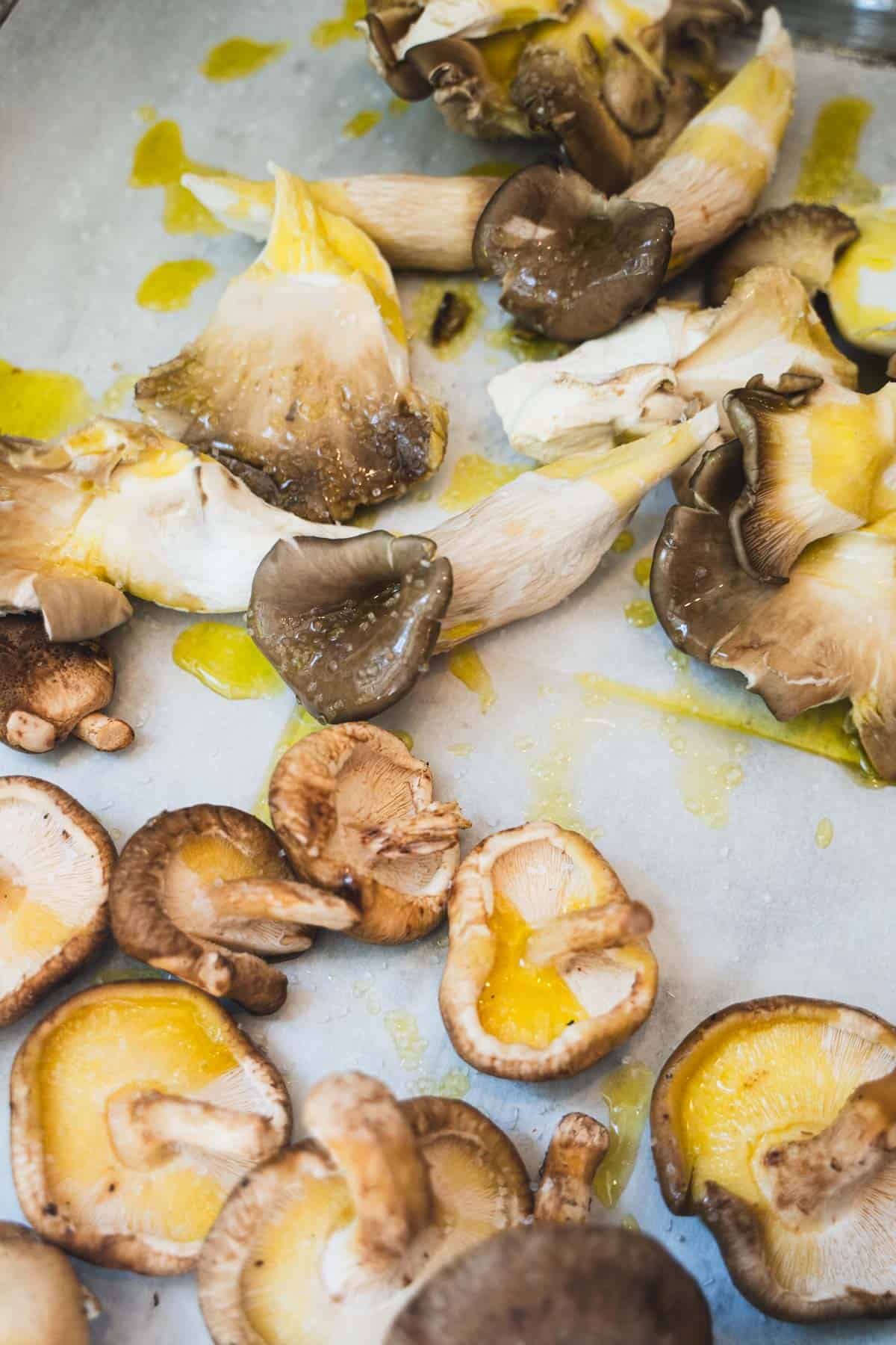 Mix of oyster and shitake mushrooms on parchment paper lined baking sheet drizzled with oilive oil.
