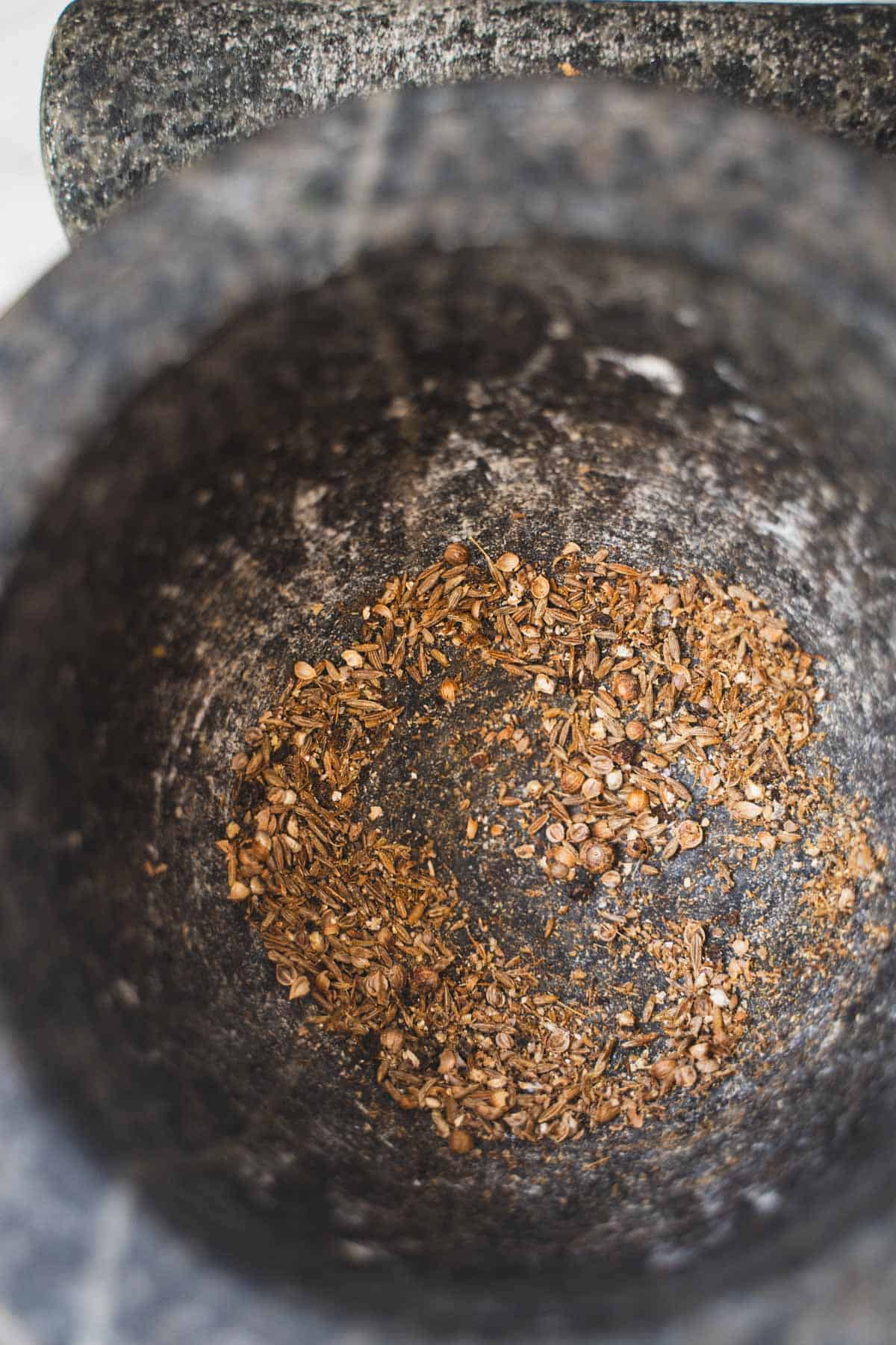 Crushed spices to make spiced balsamic vinaigrette for Mushroom salad with roasted mushrooms in mortar and pestle bowl.