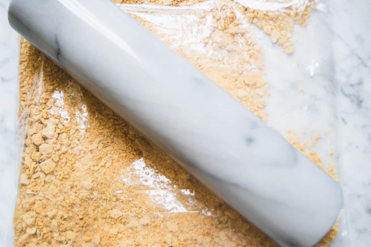 Crushed graham crackers in a zip lock bag with a rolling pin on top of the bag.
