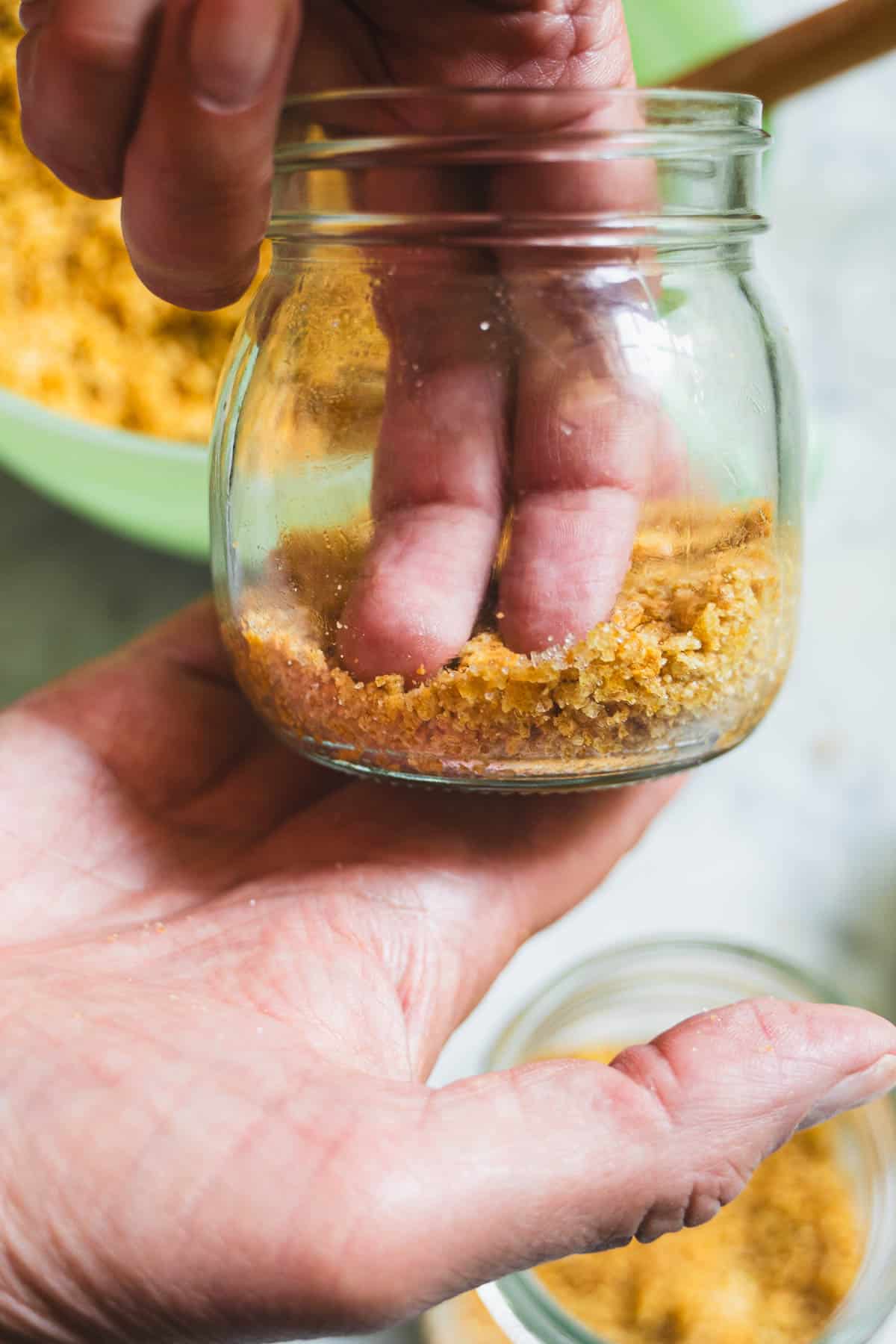 Two fingers pressing graham cracker crumbs into the bottom of a mason jar.