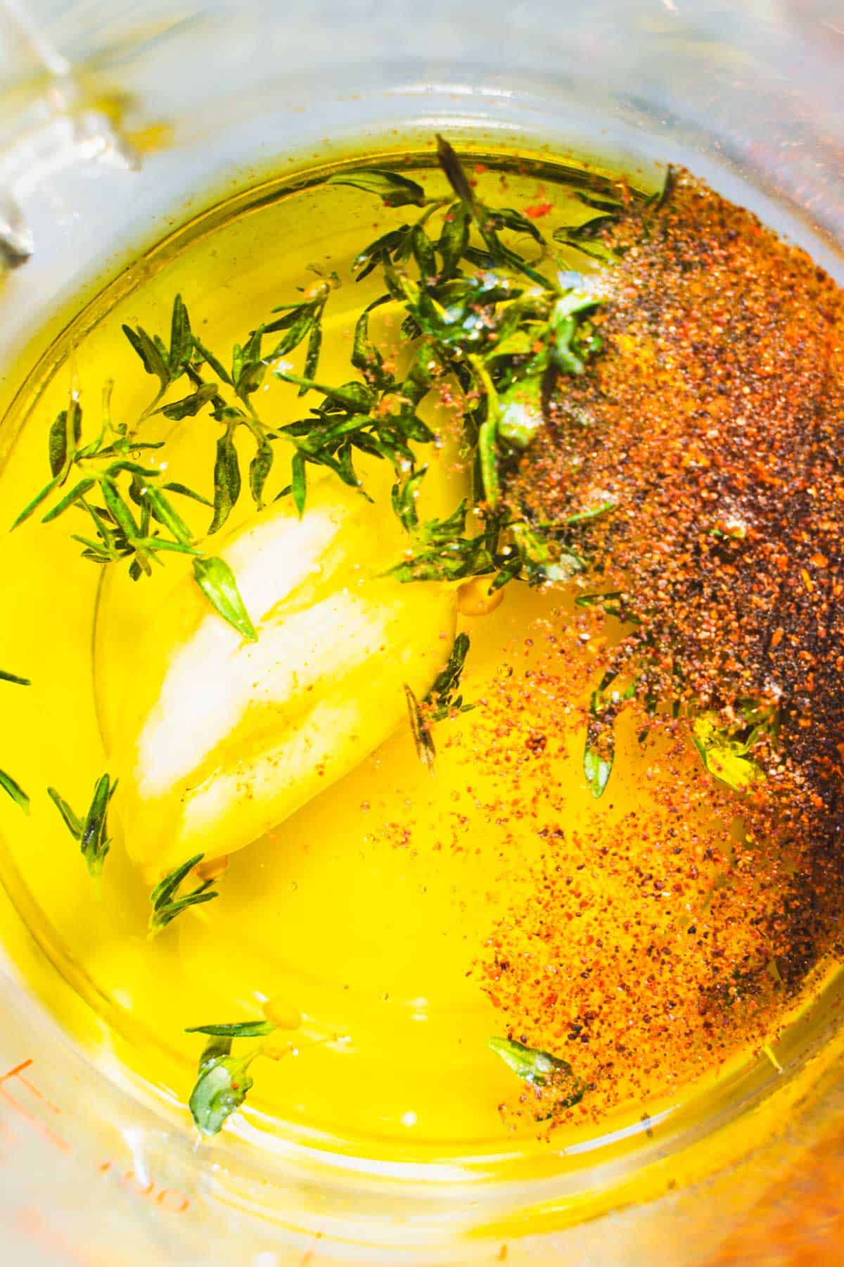 Olive oil, fresh thyme, honey, chili powder, garlic, salt and pepper in a pyrex glass measuring cup.