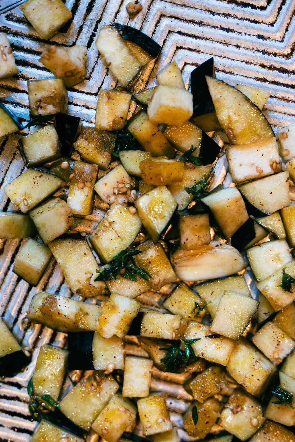 Eggplant cubes tossed in oil mixture on a baking sheet.