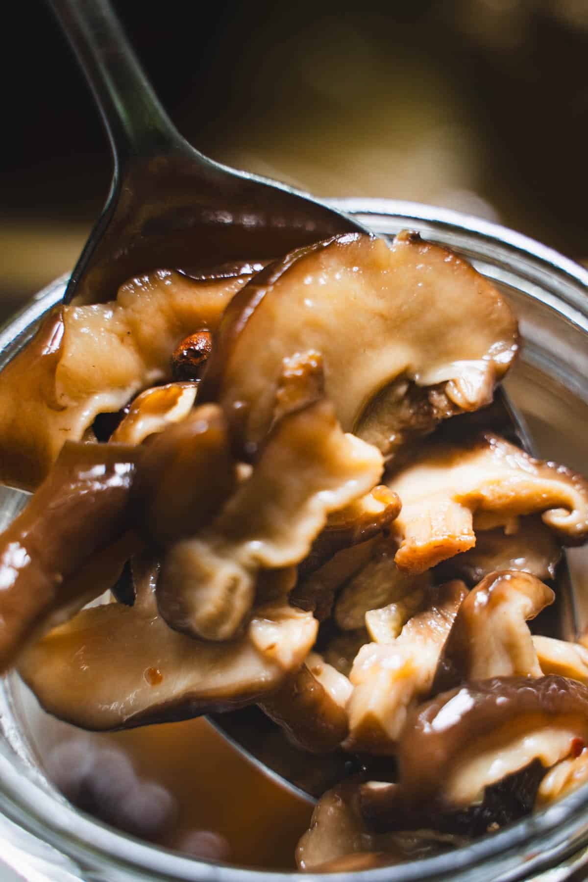 Pickled mushrooms on a spoon over a glass jar.