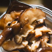 Pickled mushrooms on a spoon over a glass jar.