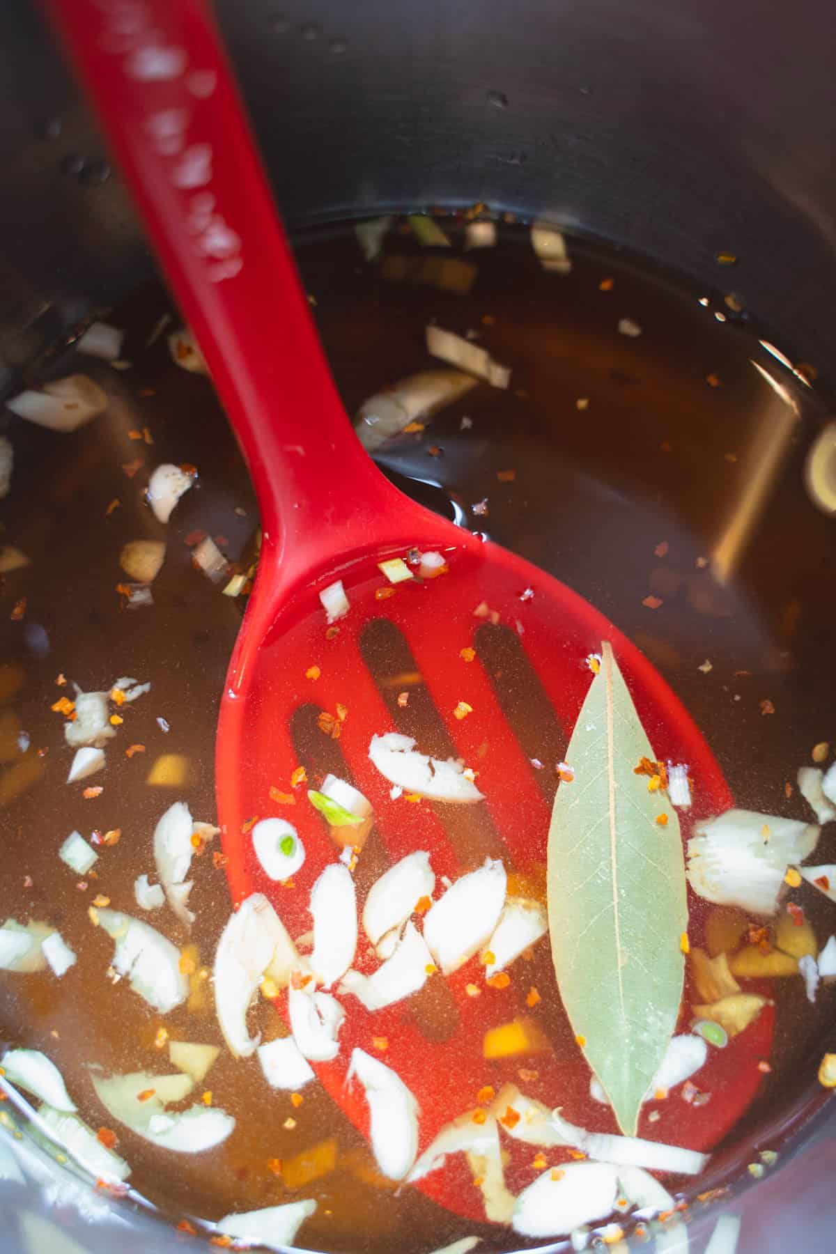 Spiced apple cider vinegar pickling brine for mushrooms in a saucepan with a red slotted spoon