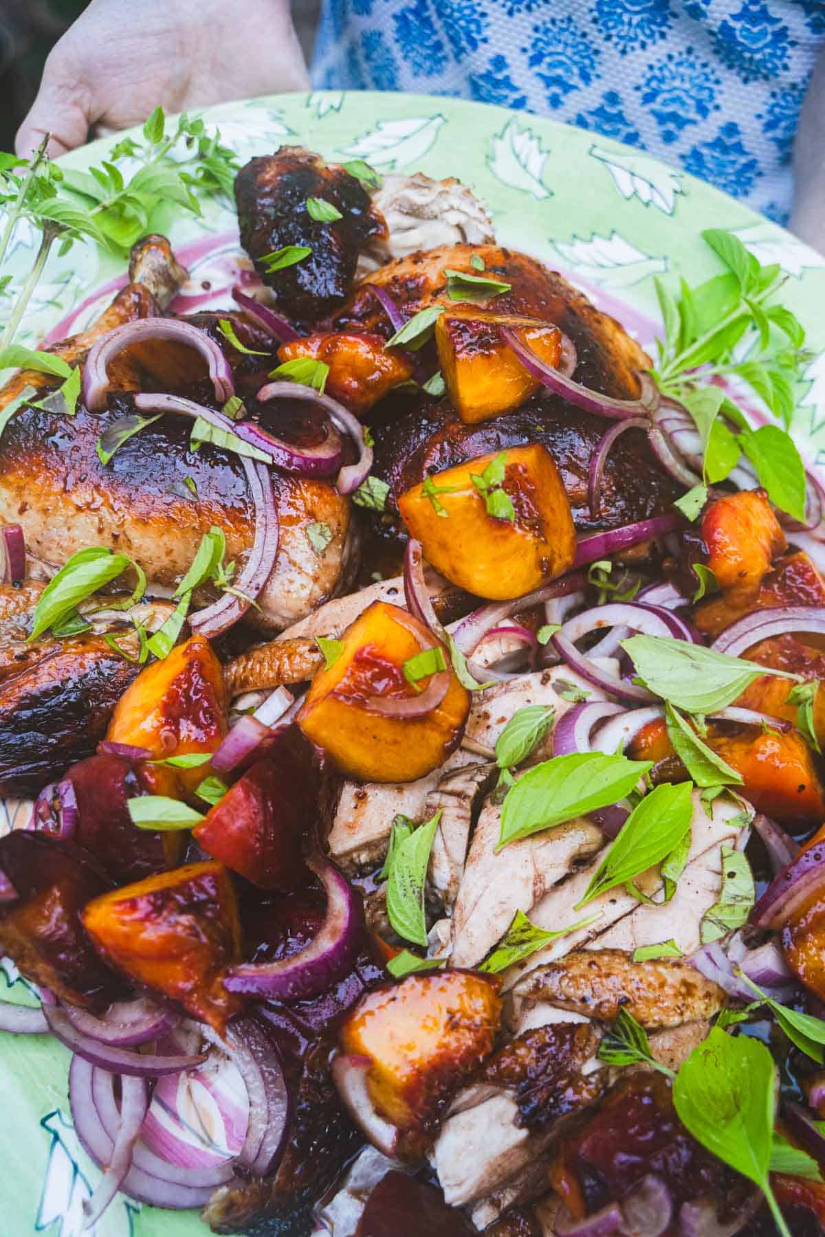 Carved spatchcock chicken with grilled peaches and basil on a serving platter.