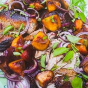 carved balsamic grilled spatchcock chicken with grilled peaches and onion sprinkled with basil on green platter.