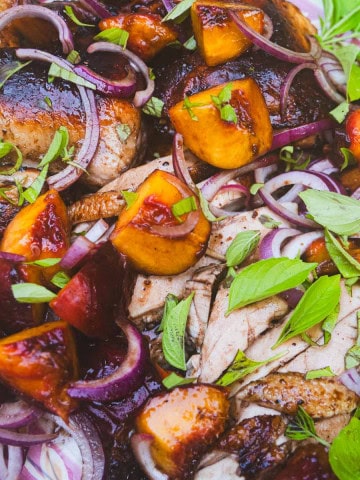 carved balsamic grilled spatchcock chicken with grilled peaches and onion sprinkled with basil on green platter.