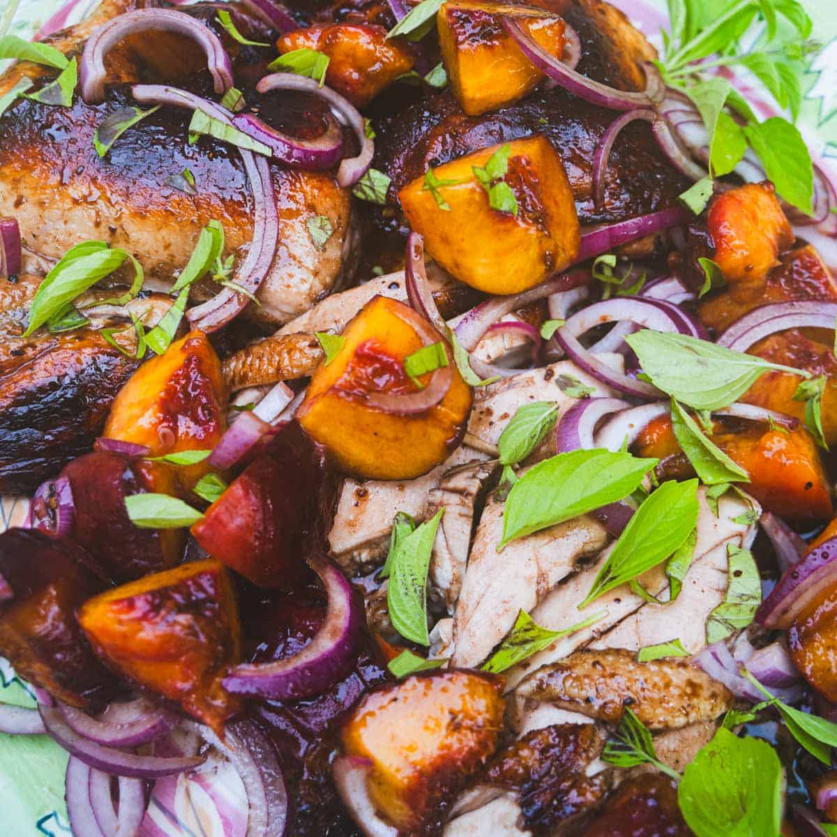 carved balsamic grilled spatchcock chicken with grilled peaches and onion sprinkled with basil on green platter.