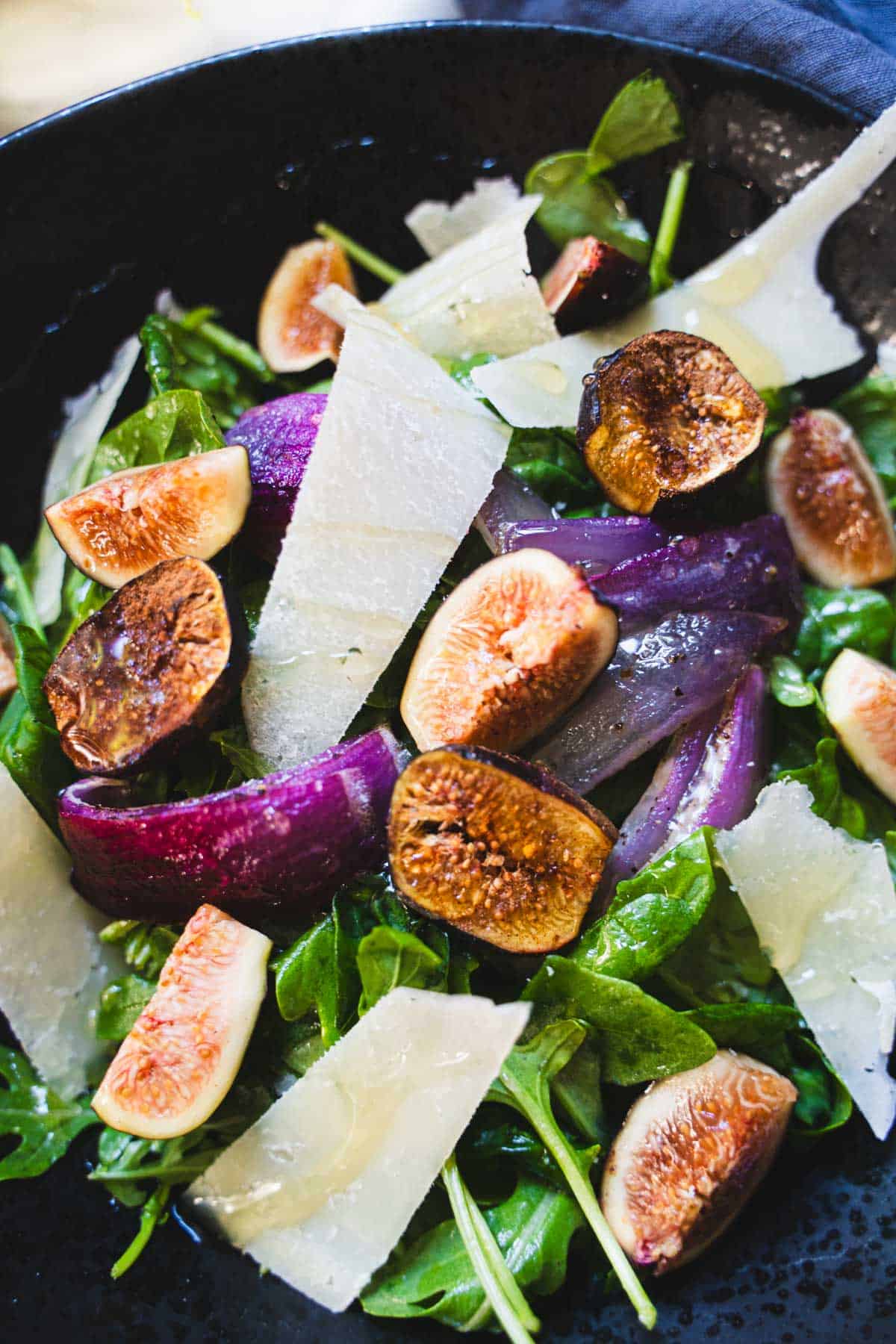 Fig salad with white balsamic dressing and shaved pecorino in a black bowl.