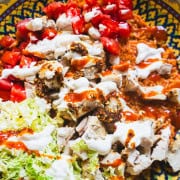 halal style chicken and yellow rice with white sauce and halal hot sauce, diced tomatoes and shredded napa cabbage in a yellow serving bowl.