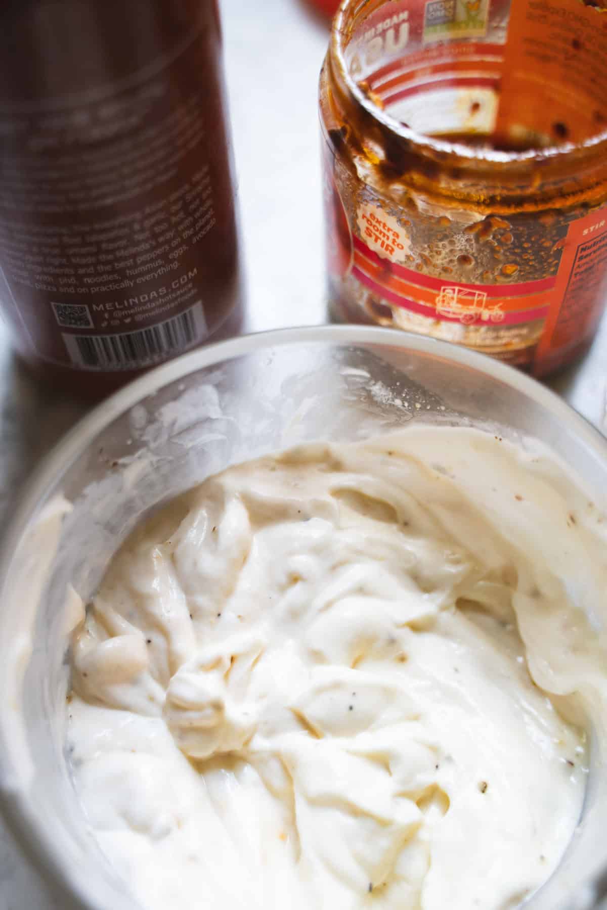 Halal white sauce in a clear beaker next to a bottle of hot sauce and chili crisp.