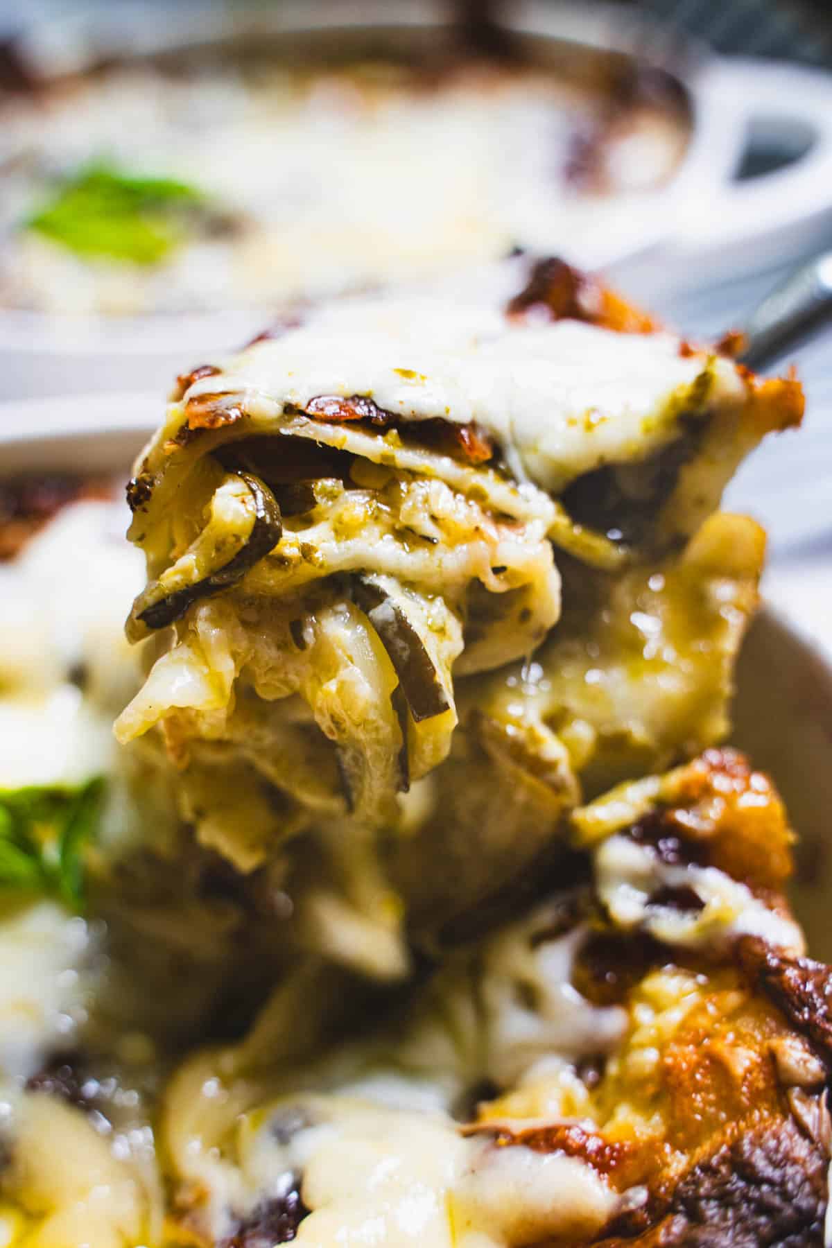 Zucchini lasagna with white sauce on a spoon above individual ramekin.