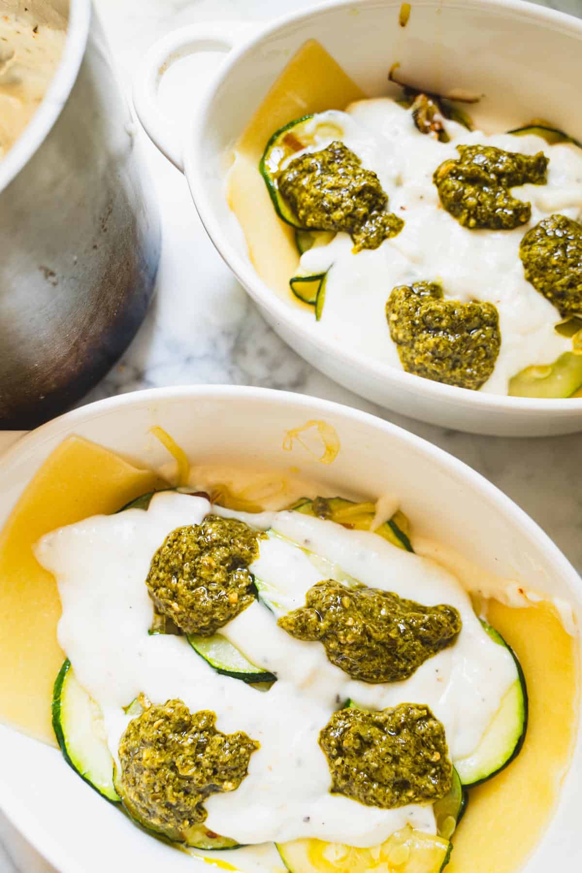 Pesto and bechamel on top of zucchini mixture layer in white ramekin.
