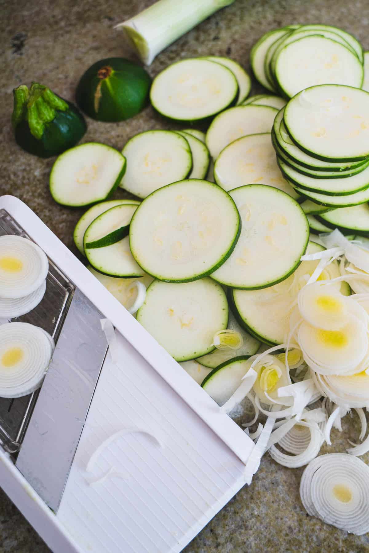 Zucchini and leeks sliced thinly with mandolin on green counter.