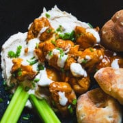 Buffalo chicken hummus bowl in a black bowl garnished with celery sticks and pita rounds next to a small bowl of blue cheese dip.