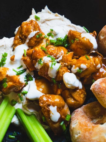 Buffalo chicken hummus bowl in a black bowl garnished with celery sticks and pita rounds next to a small bowl of blue cheese dip.