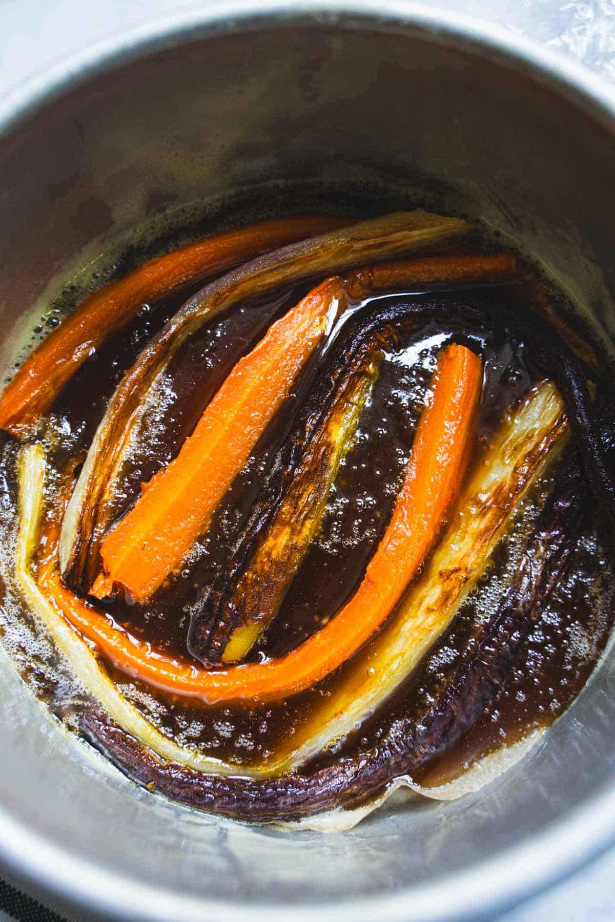 Roasted halved carrots arranged on the bottom of a 6 inch round cake pan in a maple caramel.