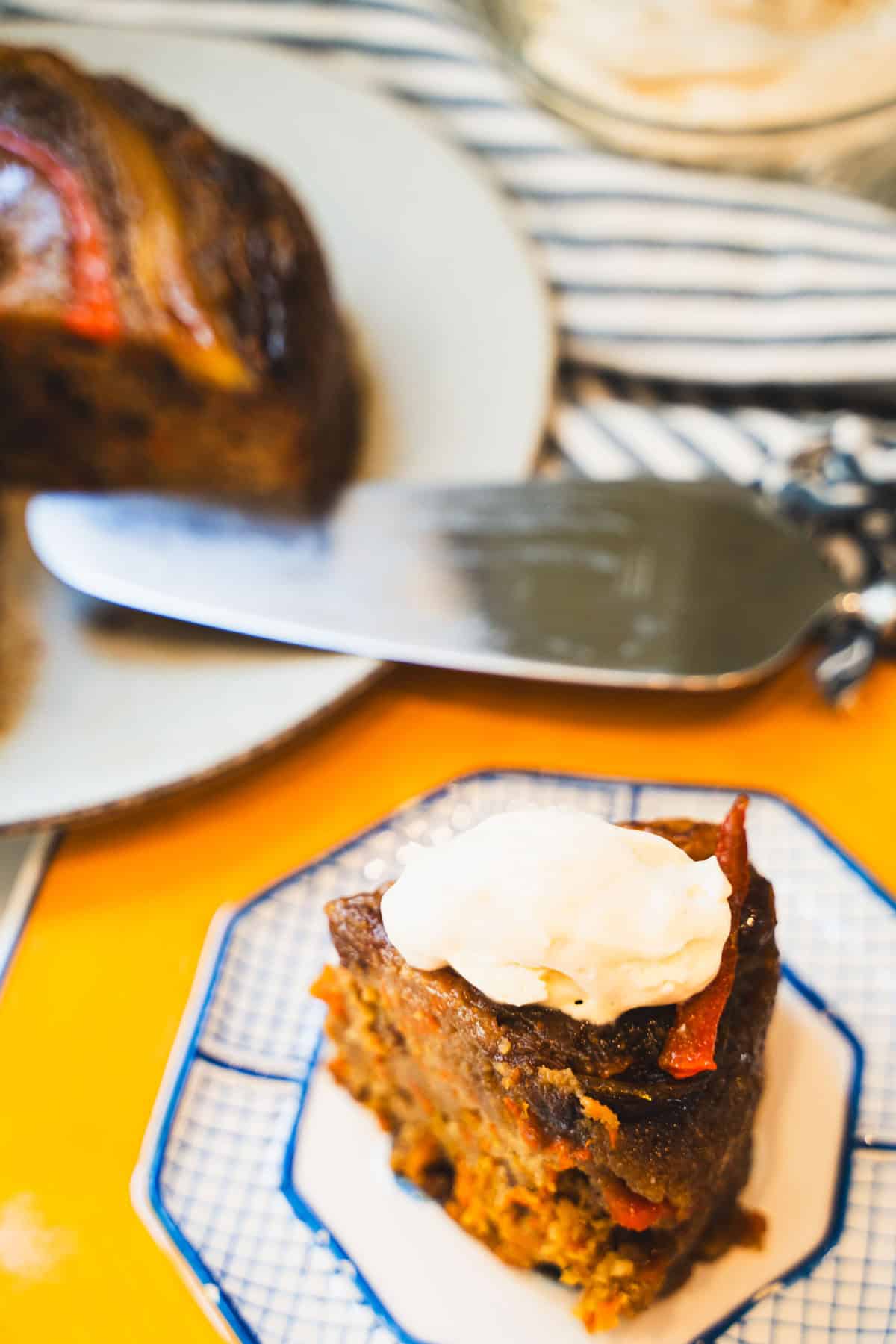 Cream cheese whipped cream dollop on top of a slice of carrot upside down cake on a yellow plate.