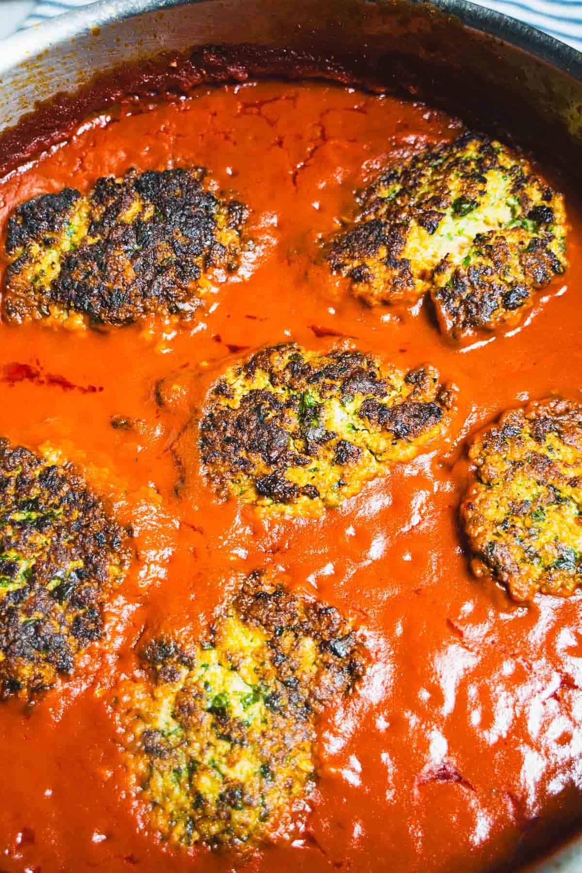 Cod cakes in tomato sauce in a sauce pan.