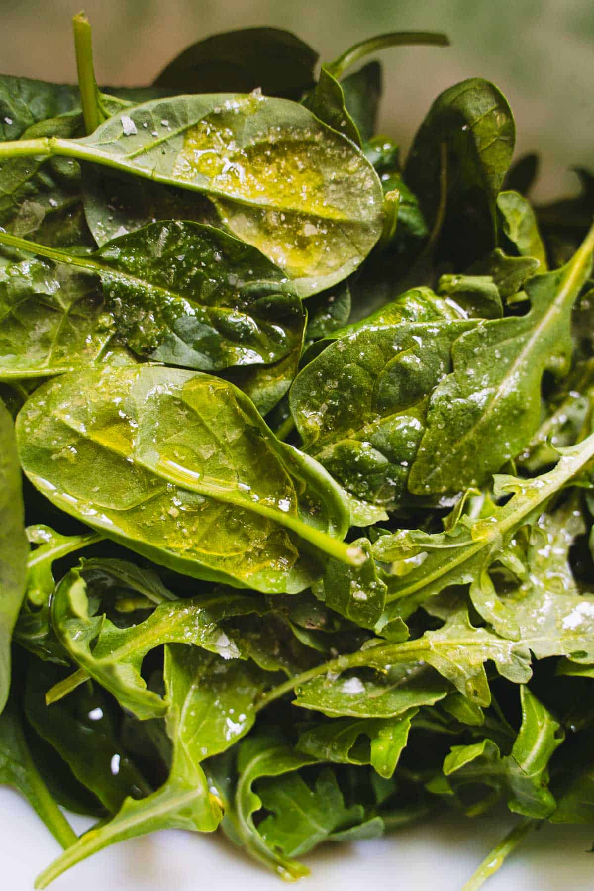 Spinach, arugula, basil dressed with white balsamic dressing in a white bowl.
