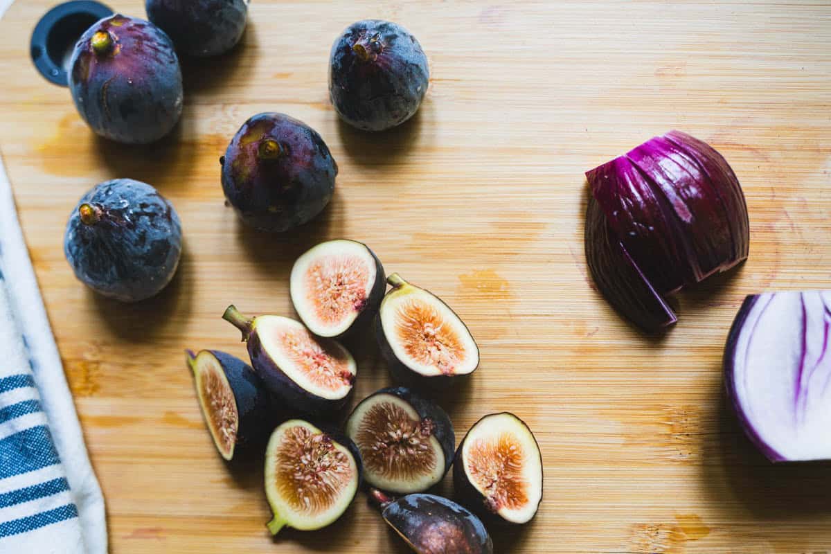 Fresh whole and halved figs alongside aa red onion halved on a cutting board.