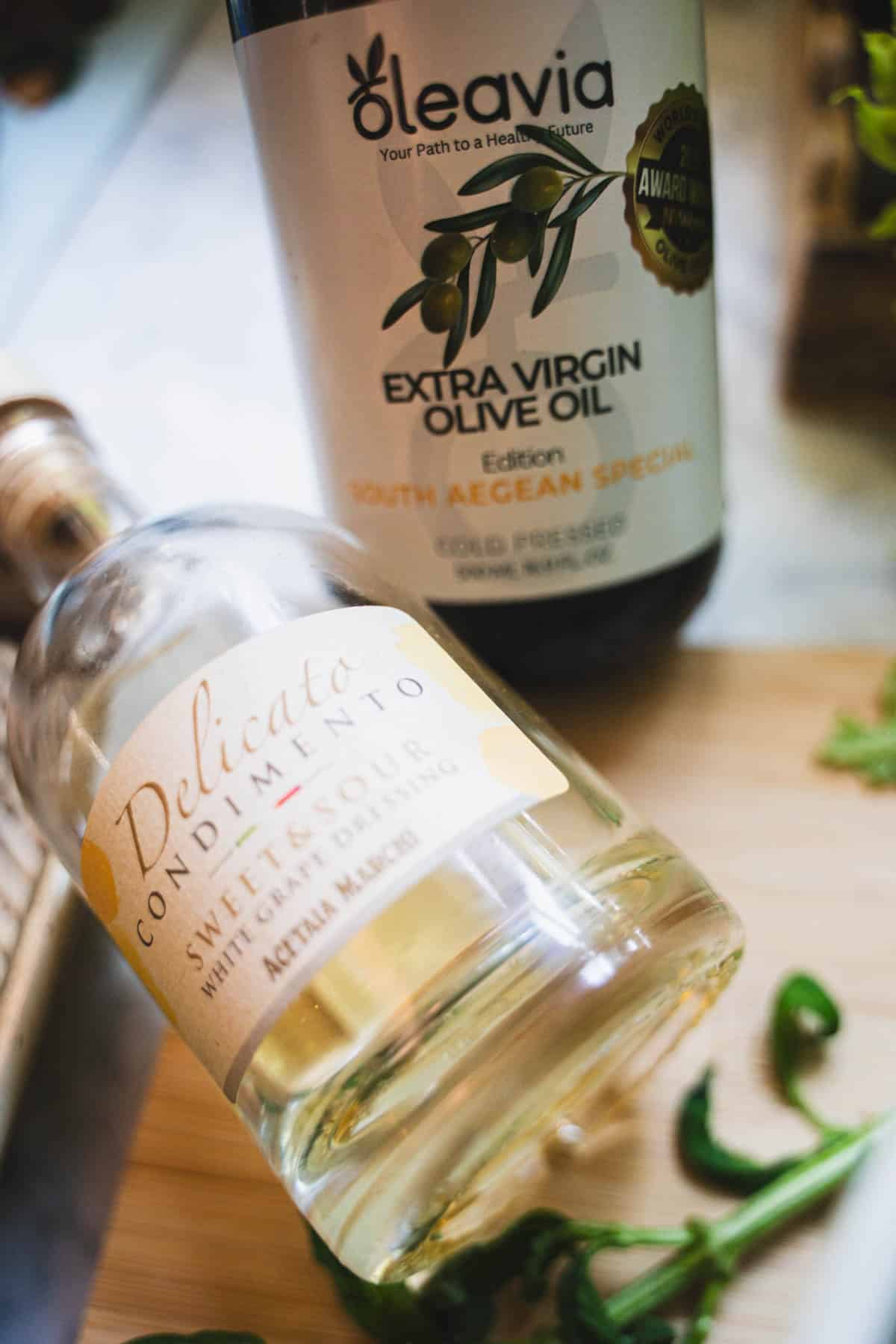 white balsamic vinegar and extra virgin olive oil bottles on cutting board to make white balsamic dressing.