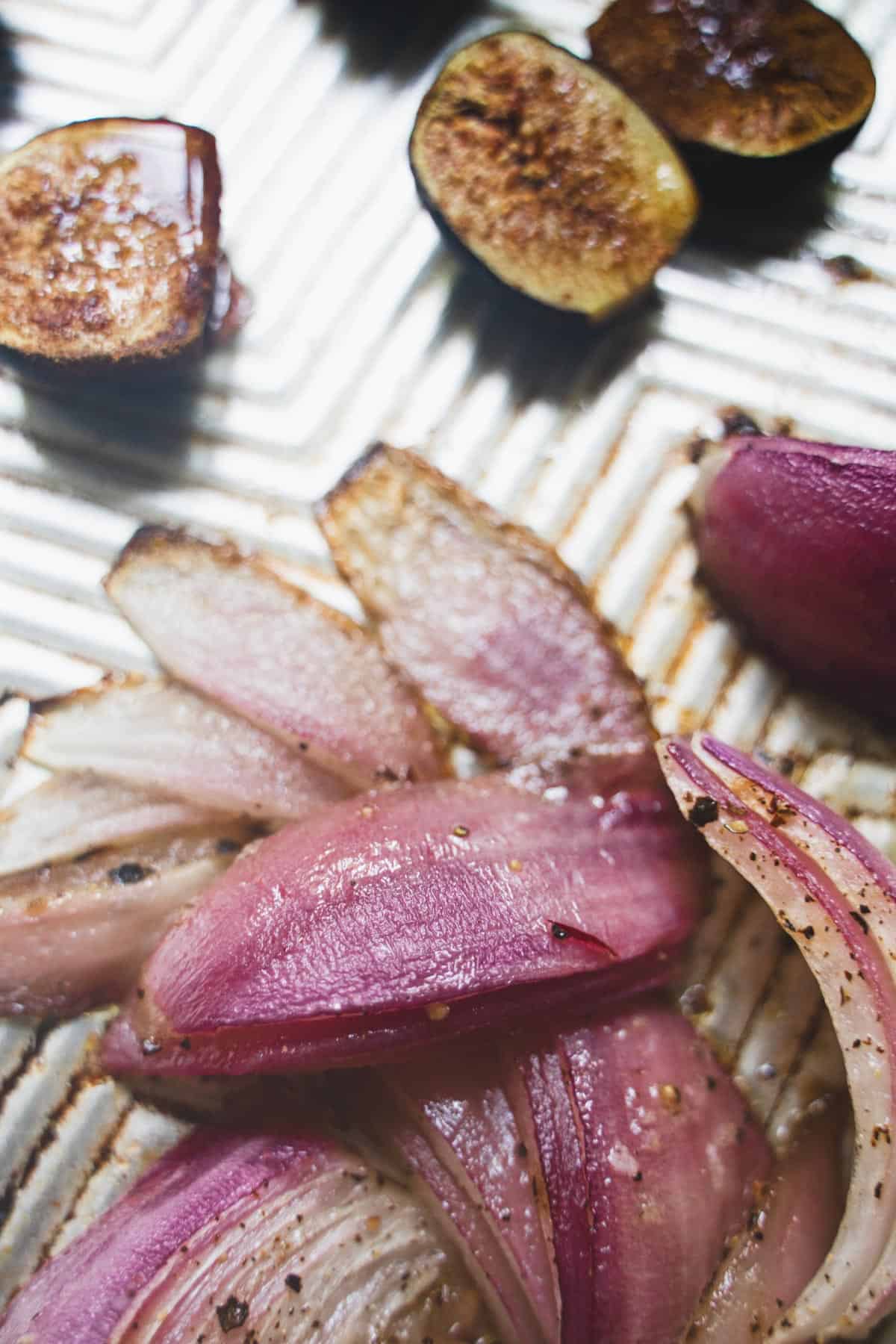 Roasted fresh figs and onion on a baking sheet.