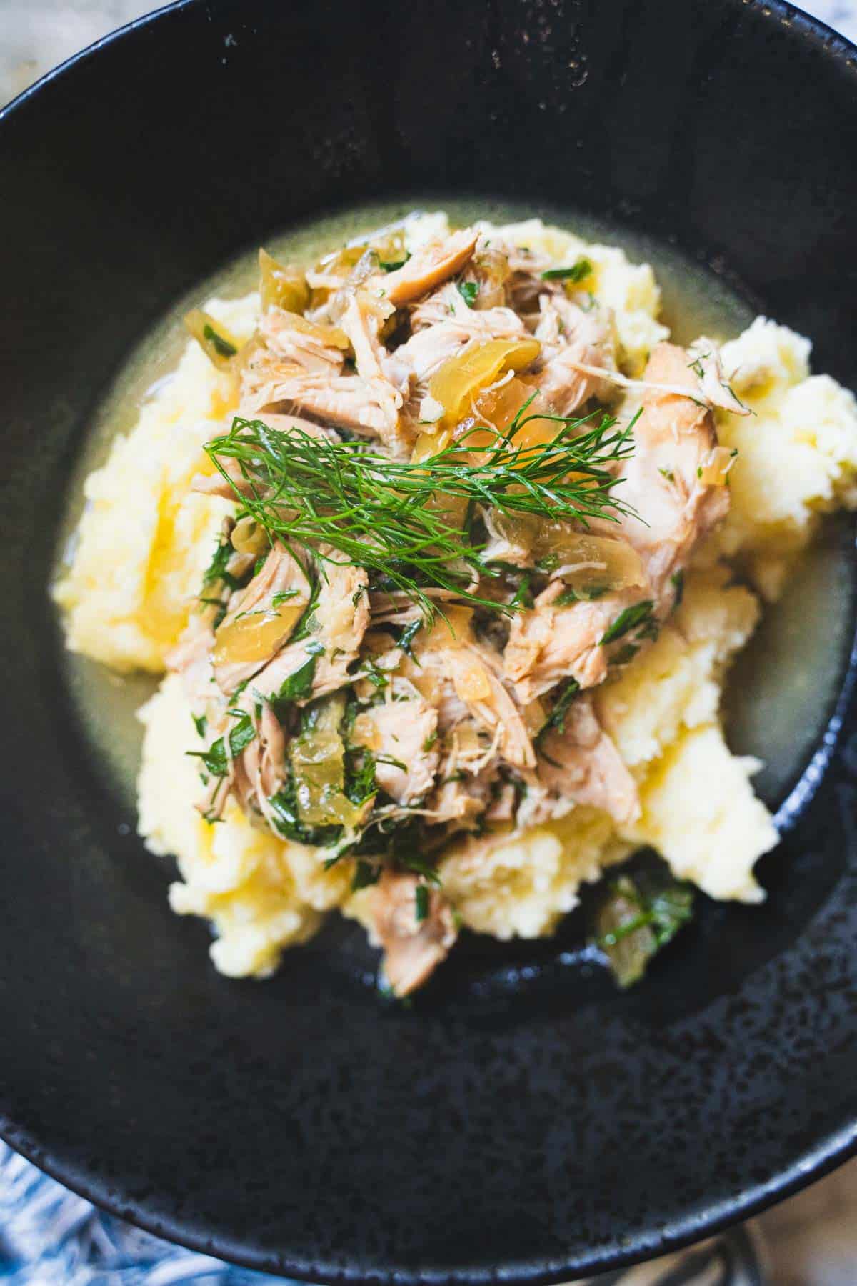 mississippi chicken with dill and chicken stock gravy over a bed of mashed potatoes in a black bowl.