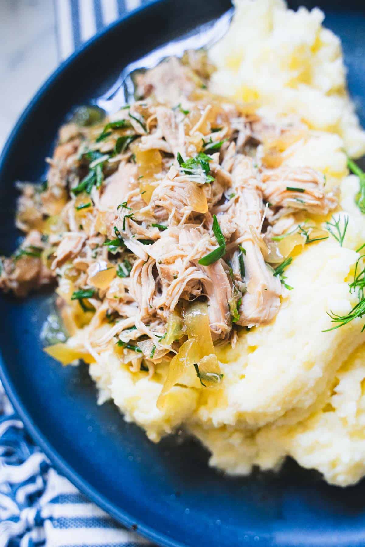 Mississippi Chicken served over a bed of mashed potatoes on a blue plate.