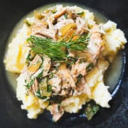 Mississippi chicken with dill and chicken stock gravy over a bed of mashed potatoes in a black bowl.