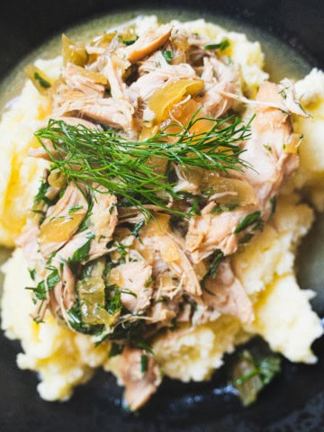 Mississippi chicken with dill and chicken stock gravy over a bed of mashed potatoes in a black bowl.