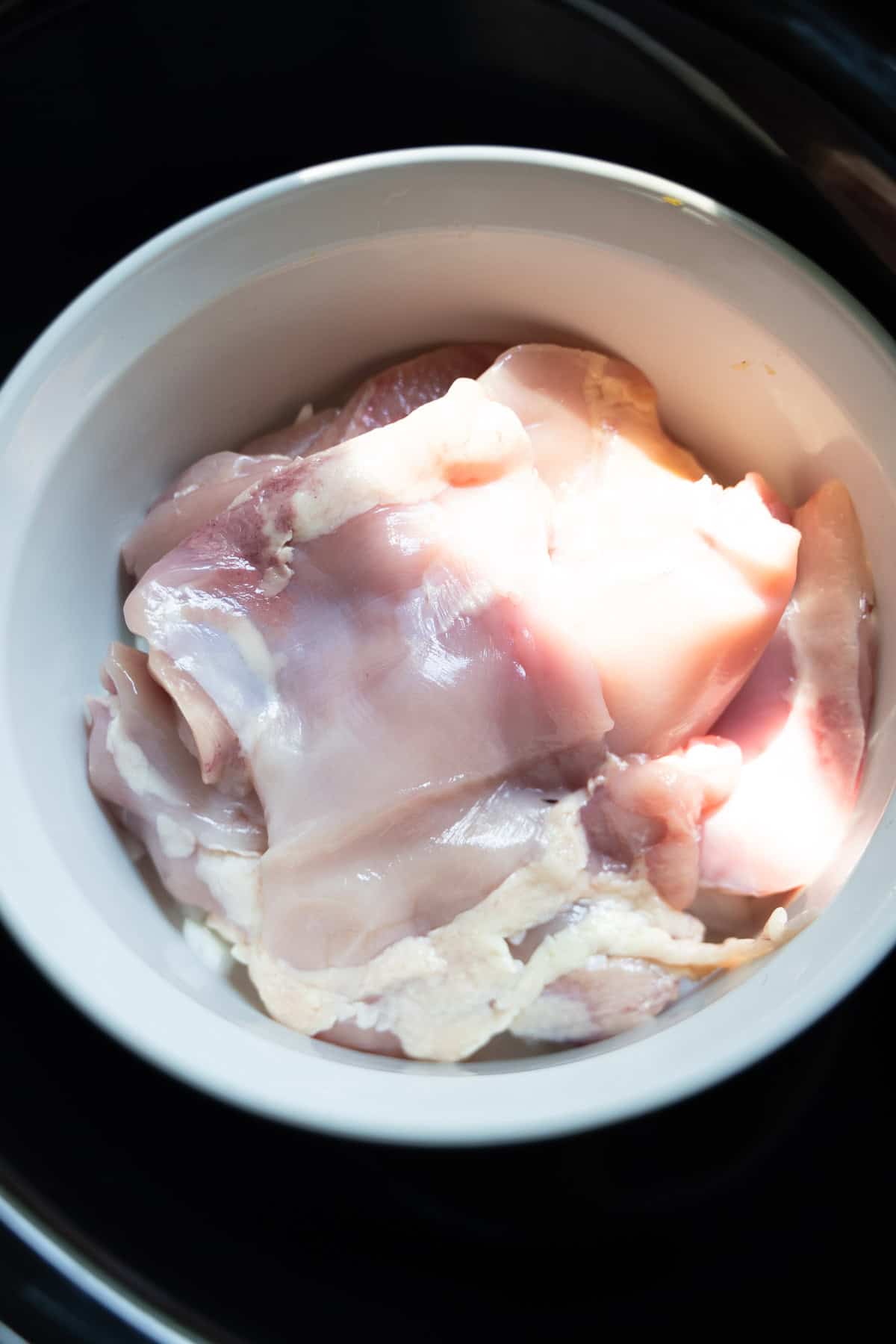 Chicken thighs layered on top of chopped onion in a baking dish that is placed inside large bowl of crock pot.
