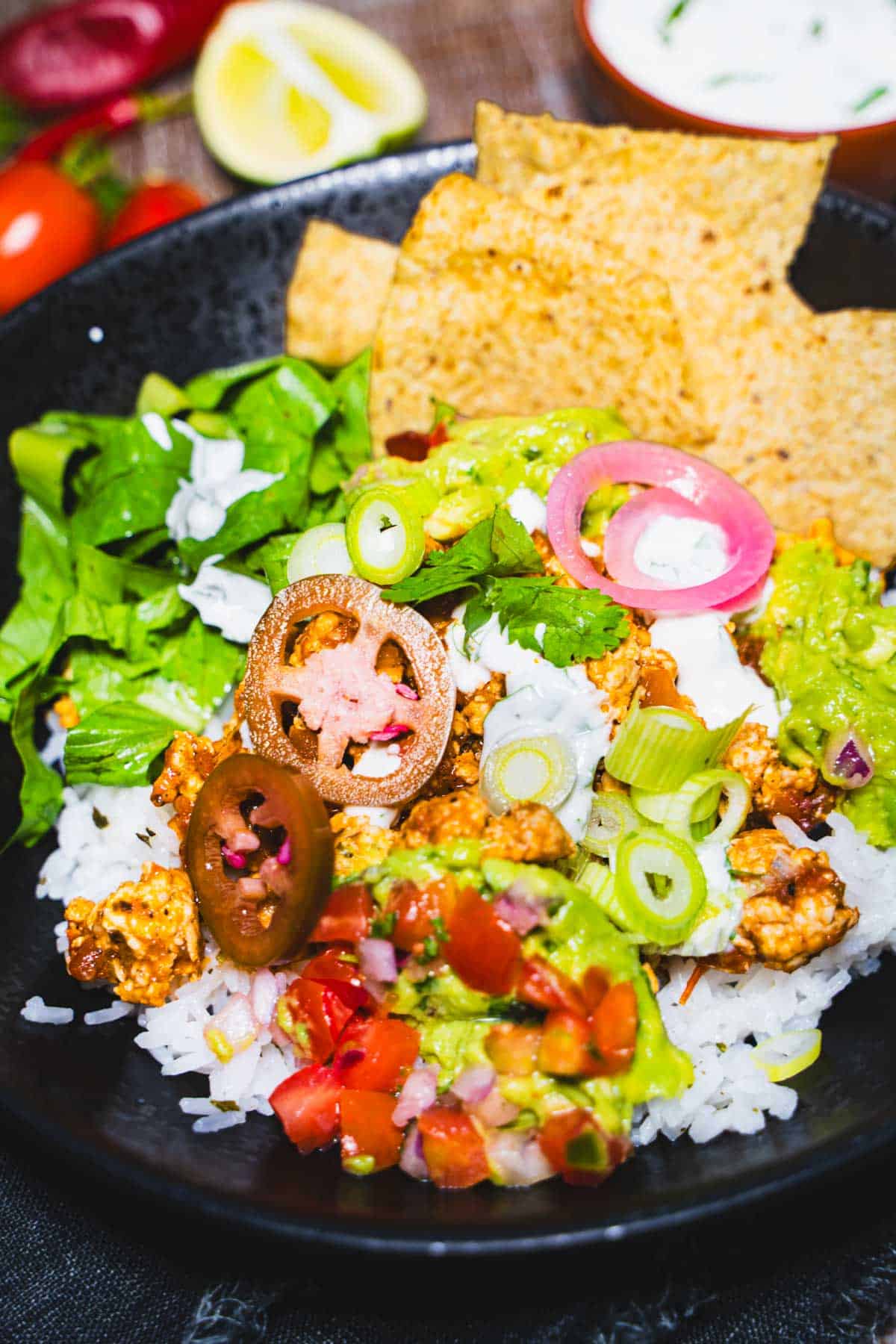 Salsa verde chicken rice bowl in a black bowl garnished with cilantro lime sauce and tortillas.