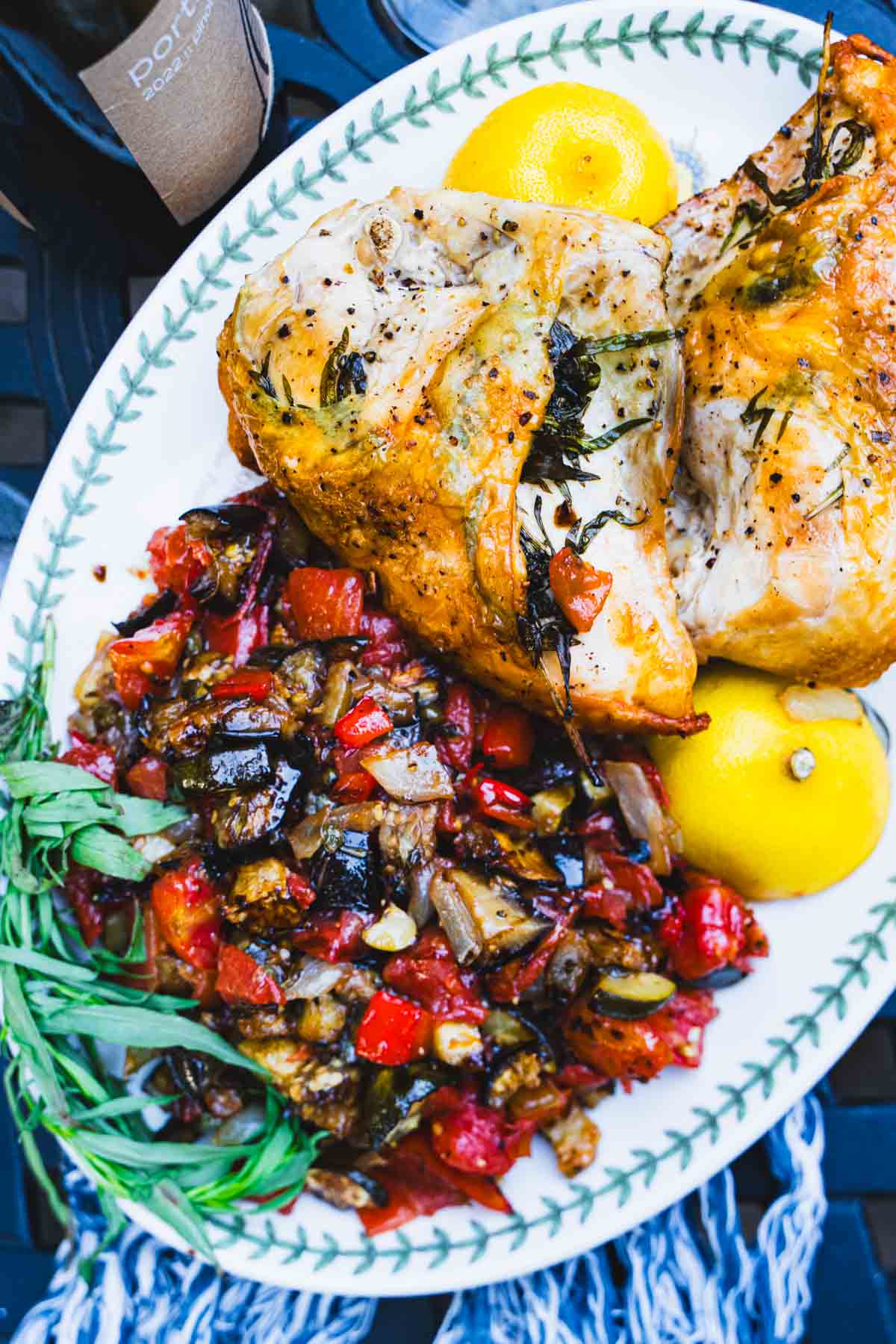 Oven roasted tarragon chicken, ratatouille and lemon on a white serving platter.
