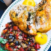 Oven roasted tarragon chicken, ratatouille and lemon on a white serving platter.