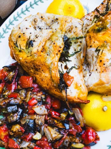 Oven roasted tarragon chicken, ratatouille and lemon on a white serving platter.