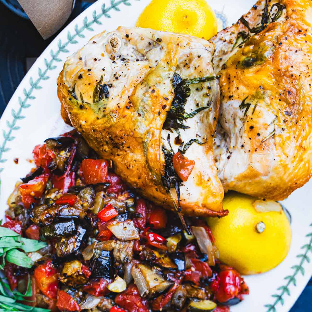 Oven roasted tarragon chicken, ratatouille and lemon on a white serving platter.